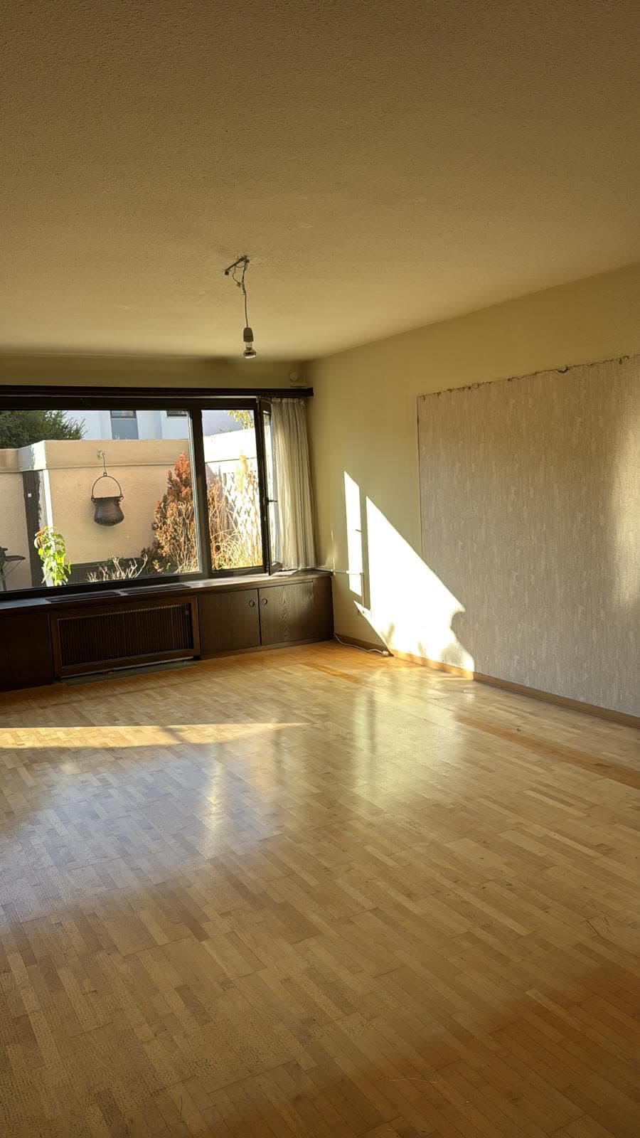 Leeres Wohnzimmer mit Parkett nach der Wohnungsauflösung, Blick zum Gartenfenster